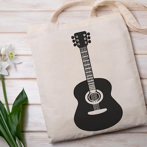 May include: A beige tote bag with a black guitar graphic. The guitar is a detailed silhouette, featuring the body, neck, and headstock. The bag has a simple design with a handle for carrying. The background is a light wooden surface.