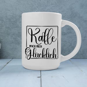 May include: White ceramic coffee mug with a black script design that reads "Kaffe MACH MICH Gl&uuml;cklich!" The mug has a large handle and is set against a light blue background. A perfect gift for coffee lovers.