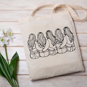 May include: A tote bag with a black and white line drawing of four women with long hair, sitting back to back with their arms around each other. The women are wearing jeans.