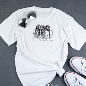 May include: White t-shirt with a black line drawing of three women with long hair, standing back to back with their arms around each other.