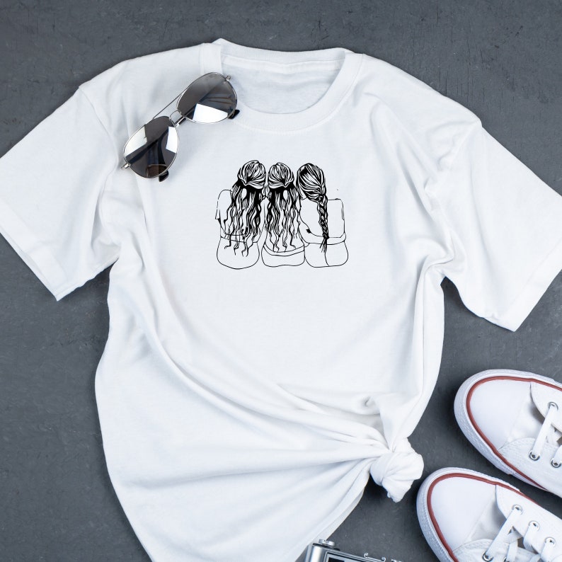 May include: White t-shirt with a black line drawing of three women with long hair, standing back to back with their arms around each other.