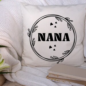 May include: White throw pillow with black text that reads "NANA" inside a circle with black floral designs and small hearts.