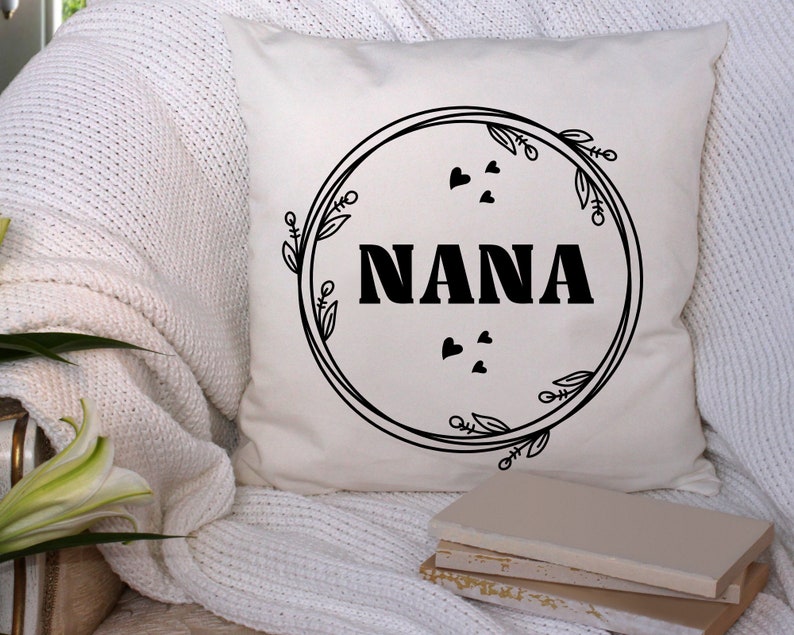 May include: White throw pillow with black text that reads "NANA" inside a circle with black floral designs and small hearts.