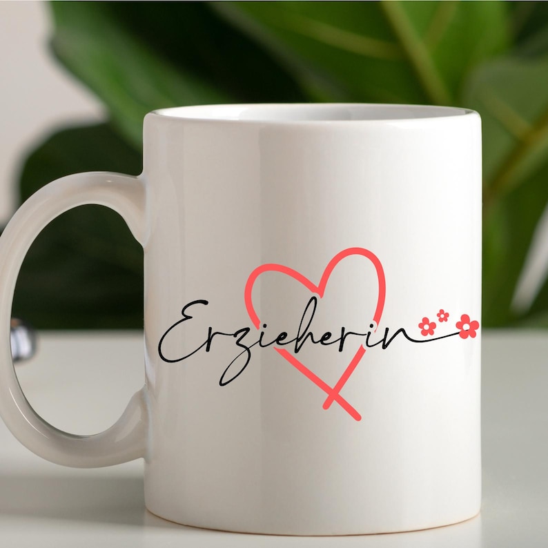 Peut inclure: Une tasse en c&eacute;ramique blanche avec une inscription cursive noire "Erzieherin" et un c&oelig;ur rose avec de petites fleurs roses.