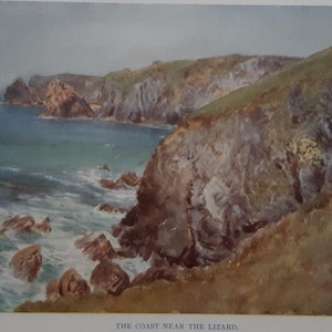 May include: A framed print of a coastal scene. The artwork shows a view of the coast with cliffs, ocean, and rocks. The cliffs are green and brown, the water is turquoise, and the sky is cloudy. The title "THE COAST NEAR THE LIZARD" is printed at the bottom.