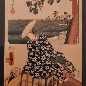 Peut inclure: Une estampe sur bois représentant une femme vêtue d'une robe à motifs noirs et blancs chevauchant un cheval. La femme porte une grande boîte sur le dos. L'arrière-plan est un paysage avec une étendue d'eau et des arbres.
