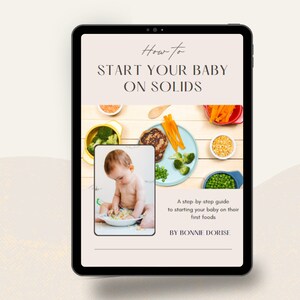 Op de afbeelding: Een digitale tablet met een gids over hoe je een baby aan vast voedsel kunt laten wennen. De gids bevat een foto van een baby die op een matje zit en met een kom eten speelt. De tekst op de tablet luidt "Hoe je je baby aan vast voedsel kunt laten wennen" en "Een stapsgewijze handleiding om je baby zijn eerste vaste voeding te geven" met de naam van de auteur, "Door Bonnie Dorise".
