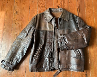 May include: A brown leather jacket with a zipper closure and a belt at the waist. The jacket has a stand-up collar and two pockets on the front.