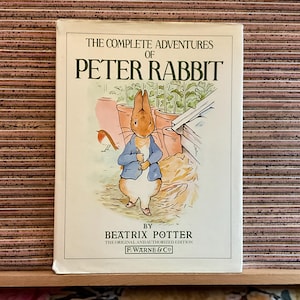 Könnte beinhalten: Ein gebundenes Buch mit dem Titel "The Complete Adventures of Peter Rabbit" von Beatrix Potter. Das Cover zeigt eine Illustration von Peter Rabbit in einer blauen Jacke in einem Garten mit einem Vogel. Originalausgabe.