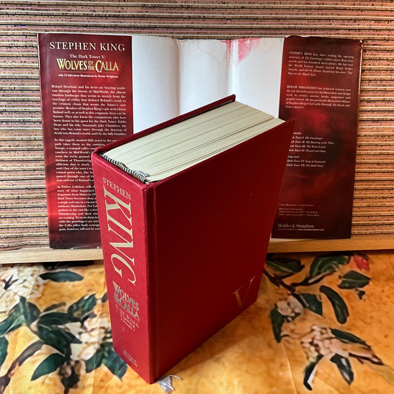 May include: A hardcover book titled "Wolves of the Calla" by Stephen King. The book has a red cover with gold lettering and a matching spine. The book is part of "The Dark Tower V" series.