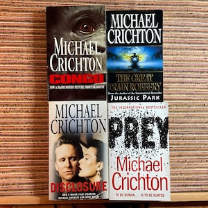 May include: Four Michael Crichton paperback books are displayed. Titles include "Congo," "The Great Train Robbery," "Disclosure," and "Prey." The book covers feature images and text in various colours, with the author's name prominent.