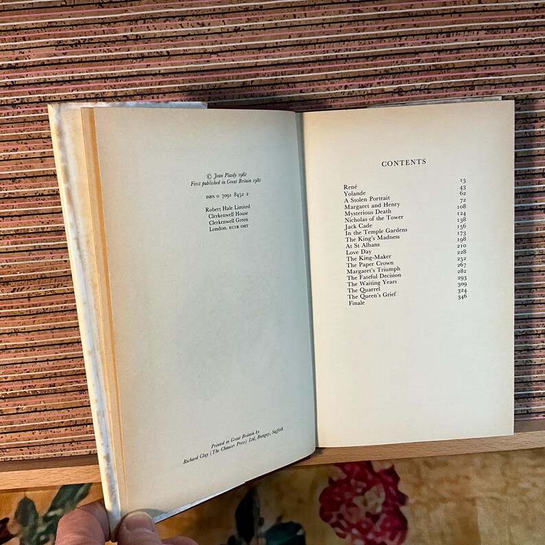 Puede incluir: Un libro abierto con p&aacute;ginas color crema. La p&aacute;gina derecha muestra una tabla de contenidos con t&iacute;tulos como "Rene" y "Yolande". La p&aacute;gina izquierda tiene texto sobre la publicaci&oacute;n del libro. El libro est&aacute; sobre una superficie de madera.