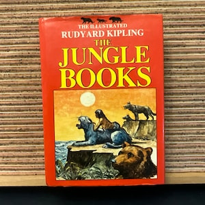 Peut inclure: Les livres de la jungle illustrés par Rudyard Kipling. La couverture présente un fond rouge avec une scène de coucher de soleil d'une panthère, d'un loup et d'un ours. Le titre est en lettres jaunes et noires.