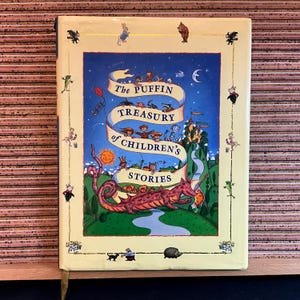 May include: A hardcover book titled "The Puffin Treasury of Children's Stories." The cover features a night sky scene with a dragon, castle, and a banner with the title. The book has a cream-colored border with small illustrations.
