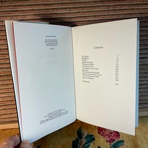 Puede incluir: Un libro abierto con p&aacute;ginas blancas, con texto y una tabla de contenidos. La p&aacute;gina izquierda muestra el t&iacute;tulo "The Kensington Queen" e informaci&oacute;n de publicaci&oacute;n. La p&aacute;gina derecha enumera los t&iacute;tulos de los cap&iacute;tulos y los n&uacute;meros de p&aacute;gina. El libro tiene un lomo rojo.