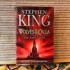 May include: A hardcover book titled "Wolves of the Calla" by Stephen King. The cover features a dark red background with a silhouetted tower and the text "The Dark Tower." The book's title and author's name are prominently displayed.