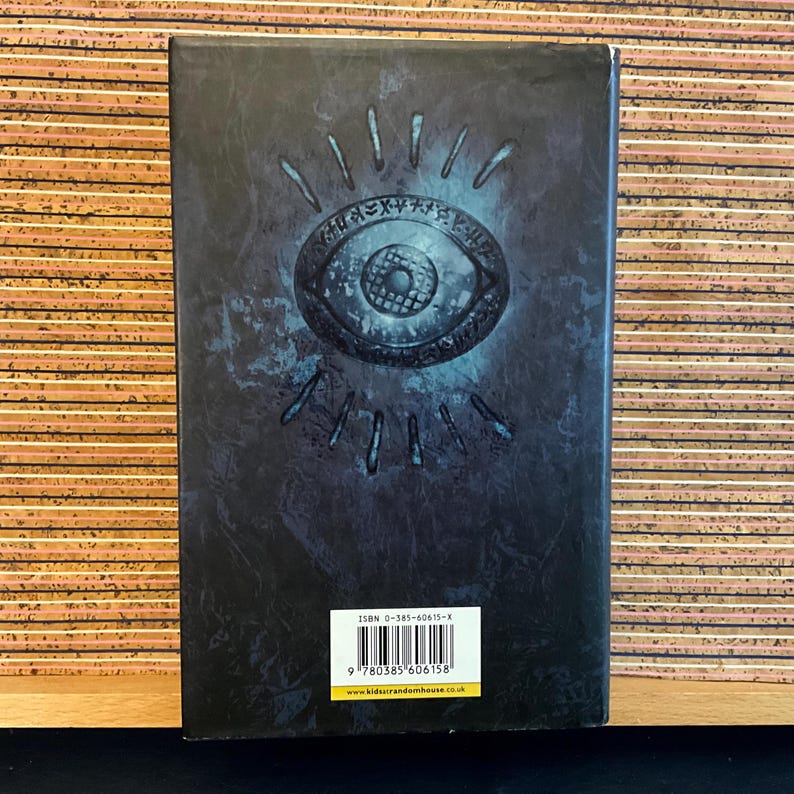 May include: A dark blue book cover with a silver eye design and a white ISBN barcode. The text on the barcode reads "ISBN 0-385-60615-X".