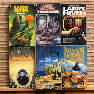 May include: Six vintage science fiction books by Larry Niven, featuring colorful covers with futuristic illustrations. Titles include "Protector," "The Ringworld Engineers," and "Crashlander." The books are arranged on a wooden surface.