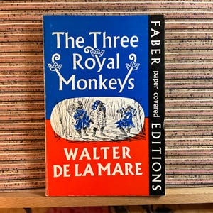 May include: A vintage book titled "The Three Royal Monkeys" by Walter De La Mare. The cover features a blue and red design with illustrations of three figures in blue and white clothing. The spine reads "FABER paper covered EDITIONS."