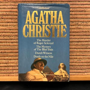 May include: A vintage paperback book titled "AGATHA CHRISTIE" in gold lettering on a blue background. The book features a portrait of a man in a hat and a sphinx illustration. Titles include "The Murder of Roger Ackroyd" and "Death on the Nile."