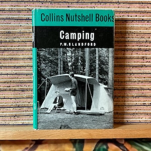 May include: A vintage book titled "Camping" by P.W. Blandford from the Collins Nutshell Books series. The cover features a black and white image of two people camping near a tent in a forest setting. The book has a teal spine.