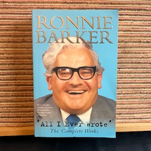 May include: A blue book cover with a photo of Ronnie Barker, a British comedian, wearing glasses and smiling. The title of the book is "All I Ever Wrote' The Complete Works".