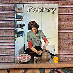 May include: A book cover titled "Pottery" features a woman working on a pottery wheel. She wears a green and white checkered shirt with red sleeves. The cover includes the text "Macdonald Guidelines Information-Activities Reference."