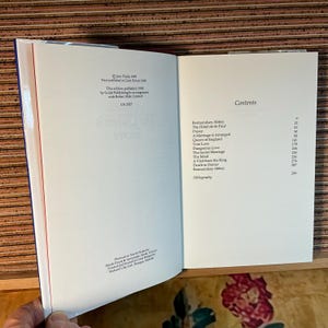 Puede incluir: Libro abierto con p&aacute;ginas blancas, que muestra texto y una tabla de contenidos. La p&aacute;gina izquierda tiene detalles de publicaci&oacute;n. La p&aacute;gina derecha enumera los t&iacute;tulos de los cap&iacute;tulos y los n&uacute;meros de p&aacute;gina. El libro est&aacute; abierto sobre una superficie de madera.