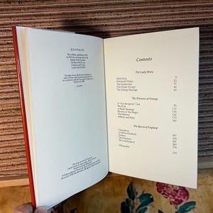 Puede incluir: Libro abierto con lomo rojo, mostrando la p&aacute;gina de contenido. La p&aacute;gina enumera cap&iacute;tulos como "The Lady Mary" y "The Princess of Orange". El texto es negro sobre fondo blanco.