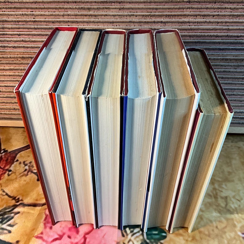 Puede incluir: Una fila de libros de tapa dura con lomos rojos, blancos y azules. Los libros est&aacute;n colocados en posici&oacute;n vertical, con sus p&aacute;ginas visibles. Los bordes de las p&aacute;ginas est&aacute;n amarillentos. Los libros est&aacute;n sobre una superficie estampada.