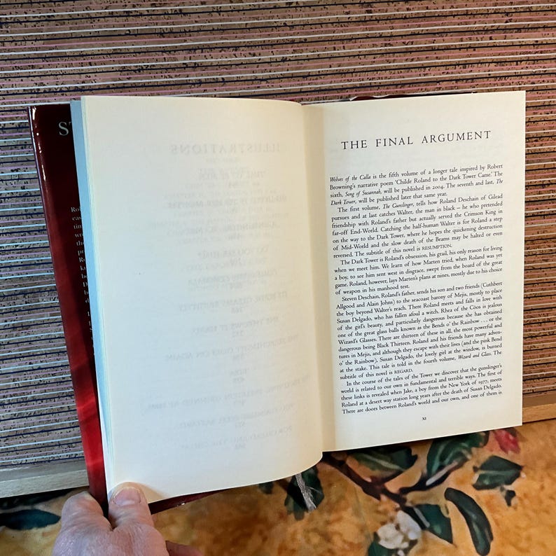 May include: An open book with text on the right page and a red cover. The text on the right page is titled "THE FINAL ARGUMENT". The left page is mostly blank. The book is held open by a hand.