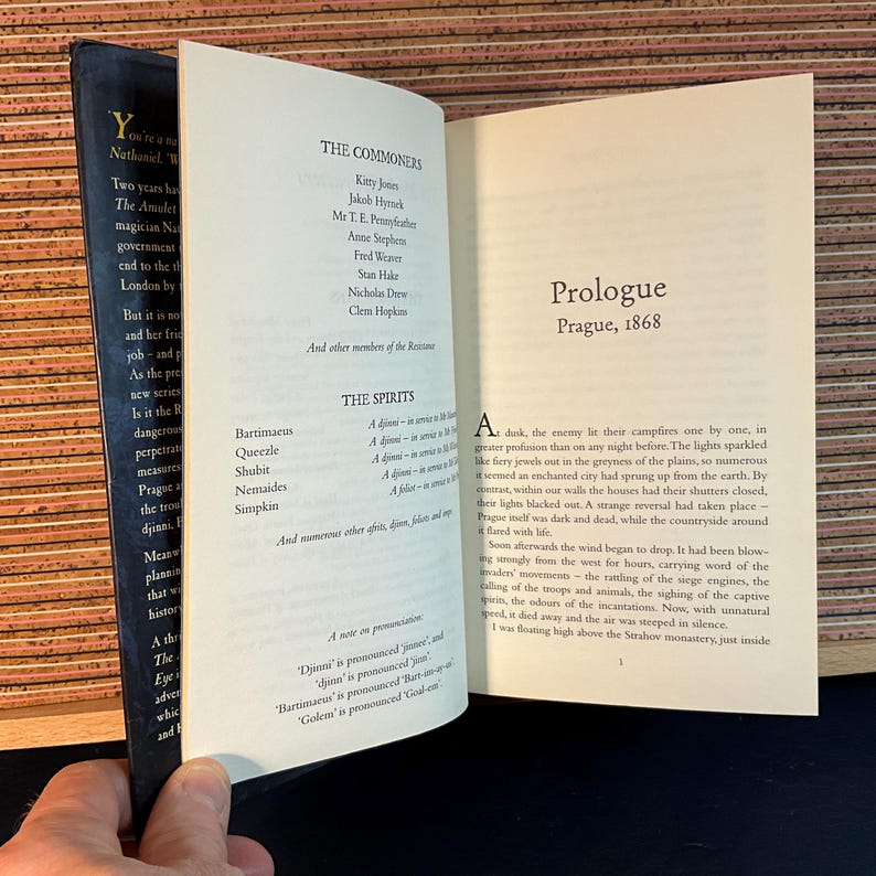 May include: An open book with a brown leather cover. The book is titled "The Commoners" and "The Spirits". The text on the page describes the characters and spirits in the book. The book is open to the prologue, which is set in Prague in 1868.