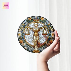 Op de afbeelding: Een rond glas-in-loodraam met een kleurrijke bloemrand en een centraal beeld van een vrouw die een weegschaal van de rechtvaardigheid vasthoudt. De vrouw draagt een vloeiende mantel en een kroon. De weegschaal is in evenwicht en de vrouw kijkt recht vooruit.