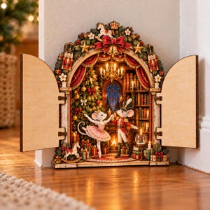 Könnte beinhalten: Ein dekorativer hölzerner Buchnischen-Einsatz mit einem Bogendurchgang und offenen Türen. Im Inneren tanzen zwei Mäuse in einem festlichen Raum mit Weihnachtsbaum, Kamin, Bücherregal, Kronleuchter und Nussknacker-Figuren am Rahmen.