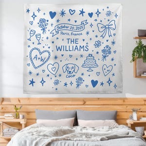 May include: White wall tapestry with blue doodle-style illustrations of hearts, flowers, stars, and a bow. Text includes "October 20, 2025, Paris, France" and "THE WILLIAMS". Features a heart with "A+W" and a dog named "Coco".