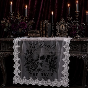 May include: A white lace table runner featuring a black graphic print of a human skull surrounded by roses. The text 'til Death' is printed above the skull, with 'THE DAVIS' and '05.19.2026' printed below the skull in a bold, dark font.