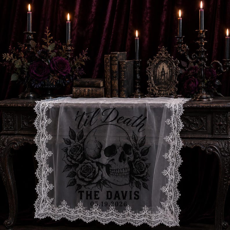May include: A white lace table runner featuring a black graphic print of a human skull surrounded by roses. The text 'til Death' is printed above the skull, with 'THE DAVIS' and '05.19.2026' printed below the skull in a bold, dark font.