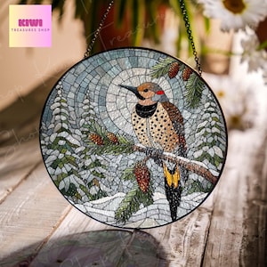 May include: A stained glass suncatcher featuring a colorful mosaic design of a woodpecker perched on a branch with pine cones. The background is a winter scene with snow-covered trees and a blue sky.