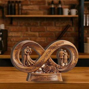 Puede incluir: Escultura de madera para el 50 aniversario de bodas. El diseño del símbolo del infinito presenta una pareja abrazándose y otra pareja de pie. La base dice "50th Wedding Anniversary 1976-2026". La escultura es marrón con detalles de rosas.