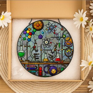 May include: A round stained glass panel depicting a science lab scene with beakers, microscopes, and atom models. The panel features a variety of colors, including green, red, yellow, and blue, and is set in a cardboard box with white padding.