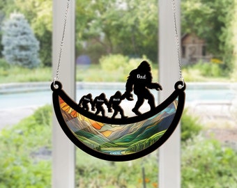 May include: A wooden crescent moon-shaped hanging ornament with a mountain scene and a family of Bigfoot figures walking across the top. The figures are labelled "Dad", "Knox", "Taden", and "Mackle".
