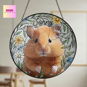 Può includere: Un acchiappasole in vetro colorato con un criceto dei cartoni animati con il nome "Sunny" scritto sopra. Il criceto è circondato da fiori e foglie in tonalità di verde, giallo e blu.