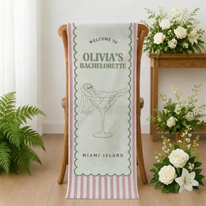 May include: A decorative table runner with a pink and white striped design and scalloped edges. The runner features the text "WELCOME TO OLIVIA'S BACHELORETTE" and a graphic of a woman in a martini glass. The text "MIAMI ISLAND" is also included.