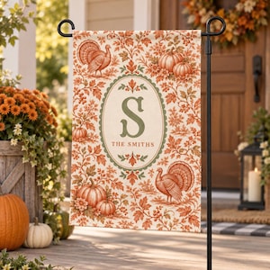 Peut inclure: Un drapeau de jardin rectangulaire orné d'un motif automnal répétitif de citrouilles orange, de dindes et de feuillage. Un cadre ovale central contient la lettre S et le texte THE SMITHS en police vert sourd sur un fond crème.