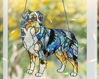 May include: A stained glass hanging ornament featuring an Australian Shepherd dog. The dog is depicted in shades of blue, black, and brown with a iridescent finish. The ornament is suspended from a silver chain.