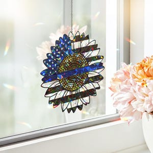 May include: A blue and white sunflower with a thin blue line across the center. The sunflower is made of iridescent material and is hanging from a window.