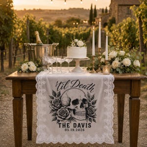 May include: A rectangular off-white table runner with white lace trim featuring a black graphic print of a human skull surrounded by roses. The text reads 'til Death', 'THE DAVIS', and '05.19.2026' in a bold, stylized black font.