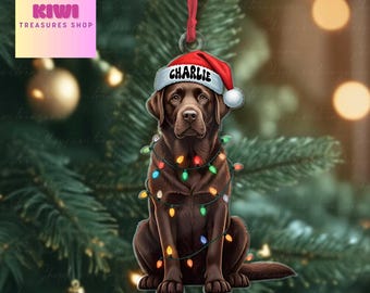 May include: A chocolate Labrador retriever Christmas ornament wearing a red and white Santa hat with the name Charlie printed on the brim. The dog is wrapped in a string of colorful glowing Christmas lights and hangs from a red ribbon.