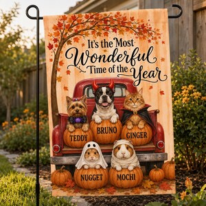 Könnte beinhalten: Eine rechteckige Gartenflagge mit einem roten Pickup-Truck und fünf Haustieren auf Kürbissen. Der Text lautet It's the Most Wonderful Time of the Year. Die Tiere sind mit Teddy, Bruno, Ginger, Nugget und Mochi beschriftet. Herbstblätter und Bäume umrahmen das Motiv.