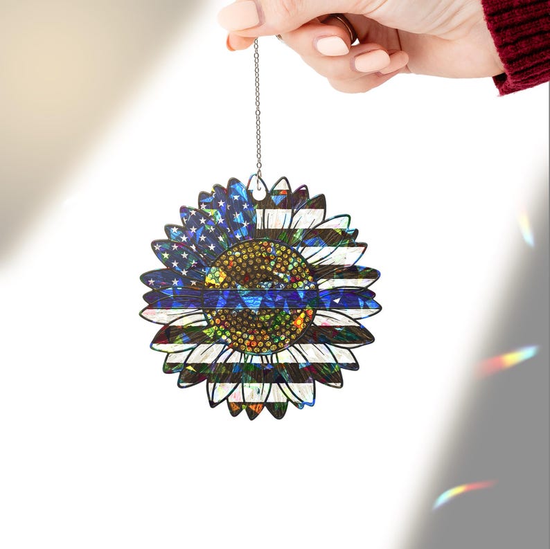 May include: A blue and white sunflower ornament with a thin blue line across the center. The sunflower is made of iridescent material and has a chain for hanging.